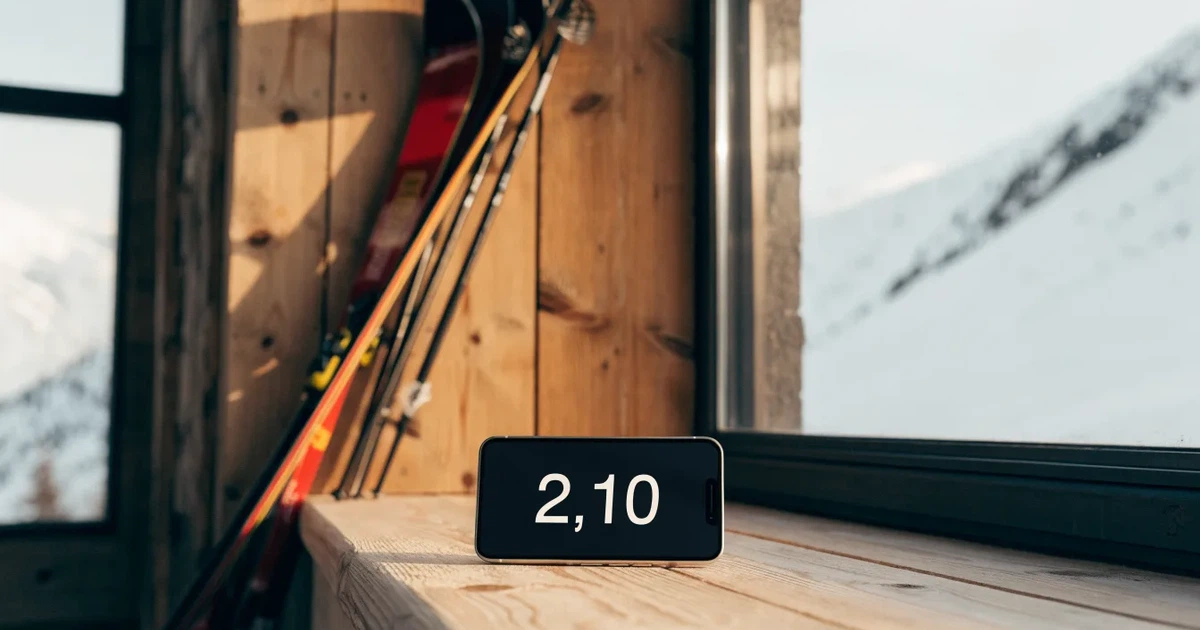 Mehrere Skier und Stöcke lehnen ordentlich in einer Reihe an der Holzwand einer Berghütte, vor dem Fenster liegt Schnee.
