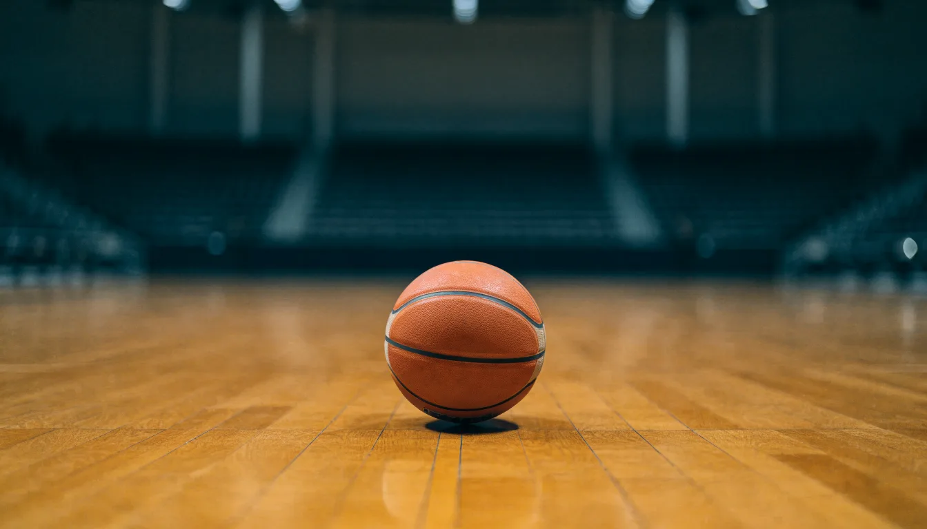 Ein Basketball liegt auf dem Parkett einer leeren Halle, von den Deckenlampen fällt gleichmässiges Licht auf den Boden.