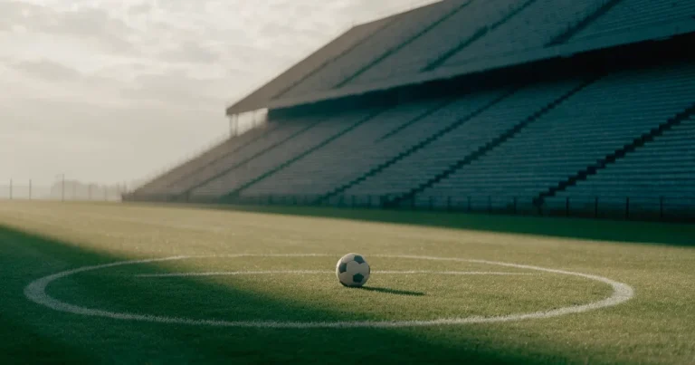 Ein Fussball liegt auf dem Anstosspunkt eines frisch gemähten Rasens, dahinter eine grosse Tribüne unter bewölktem Himmel