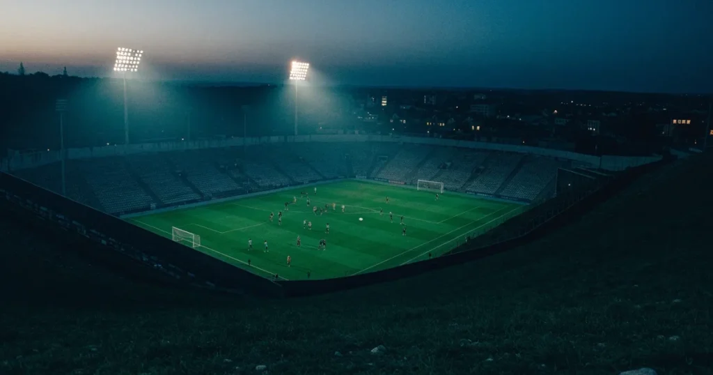 Ein Fussballstadion bei Flutlicht von einer Anhöhe aus gesehen, der Rasen leuchtet grün unter dunklem Abendhimmel