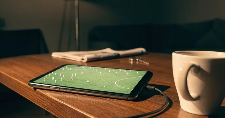 Ein Smartphone mit dunklem Display liegt auf einem Holztisch neben einem Ladekabel und einer Kaffeetasse.